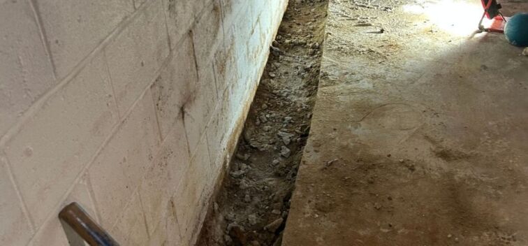Basement waterproofing trench installed along a concrete block wall to help collect and redirect groundwater away from the foundation.