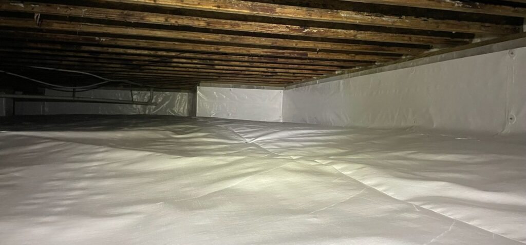 Clean crawl space with a sealed white vapor barrier installed across the floor and walls for moisture control and encapsulation.