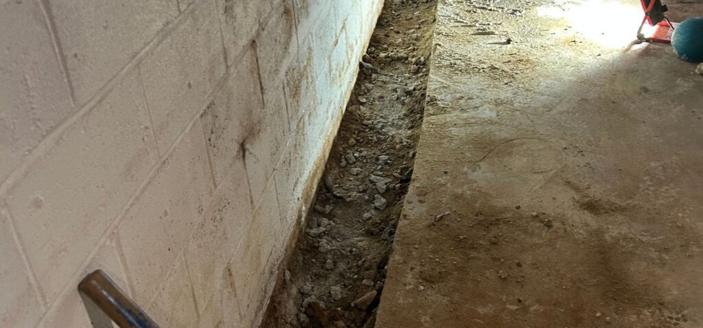 Basement waterproofing trench installed along a concrete block wall to help collect and redirect groundwater away from the foundation.